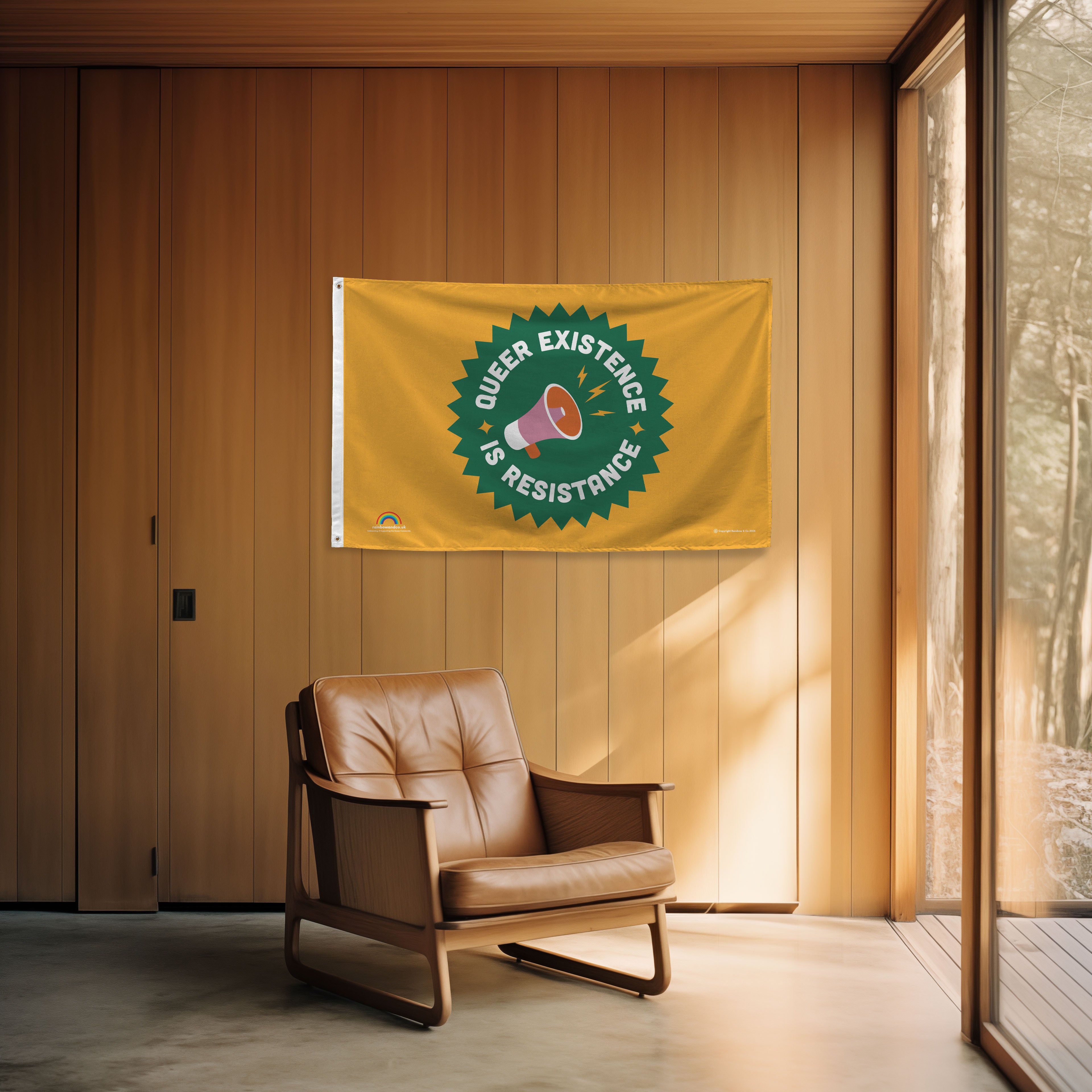 Brown leather chair in a room with a 'Queer Existence is Resistance' flag on the wall.