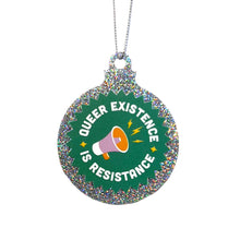 Load image into Gallery viewer, A silver glitter bauble against a white background featuring the text Queer Existence is Resistance on a green background with a graphic of a megaphone in pink and orange. It is held up by a silver string.