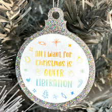 Load image into Gallery viewer, Close up of a white Christmas tree displaying a silver glitter bauble featuring the text All I Want for Christmas is QUEER LIBERATION surrounded by Christmas icons such as candy canes and stockings, all in rainbow pride colours.
