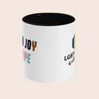 White mug with black handle and interior featuring showing the face opposite the handle. The front and back designs are slightly visible on the left and right side.