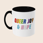 White mug with black handle and interior featuring the colourful words “Queer Joy & Hope” on the front.