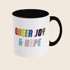 White mug with black handle and interior featuring the colourful words “Queer Joy & Hope” on the front.
