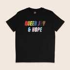 Black T-shirt with colourful text reading “Queer Joy & Hope” across the chest in rainbow and trans Pride-inspired colours.