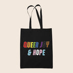 Black tote bag featuring colourful text reading “Queer Joy & Hope” in rainbow and trans Pride-inspired colours.