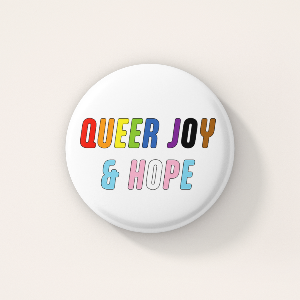 White round 38mm badge featuring the words "Queer Joy & Hope" in bold, multicoloured lettering inspired by the rainbow and transgender Pride flags.