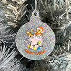 Close up of a white Christmas tree displaying a silver glitter bauble featuring retro text reading 'cosy vibes'. The image shows a mug of hot chocolate with marshmallows and a gingerbread man wearing a Santa hat. A candy cane in the mug and lights around the mug are the colours of the rainbow pride flag.