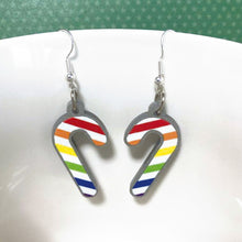 Load image into Gallery viewer, Silver glitter candy cane dangle earrings hung over the edge of a mug. The stripes on the candy cane are those of the Rainbow flag; red, orange, yellow, green, blue, purple.
