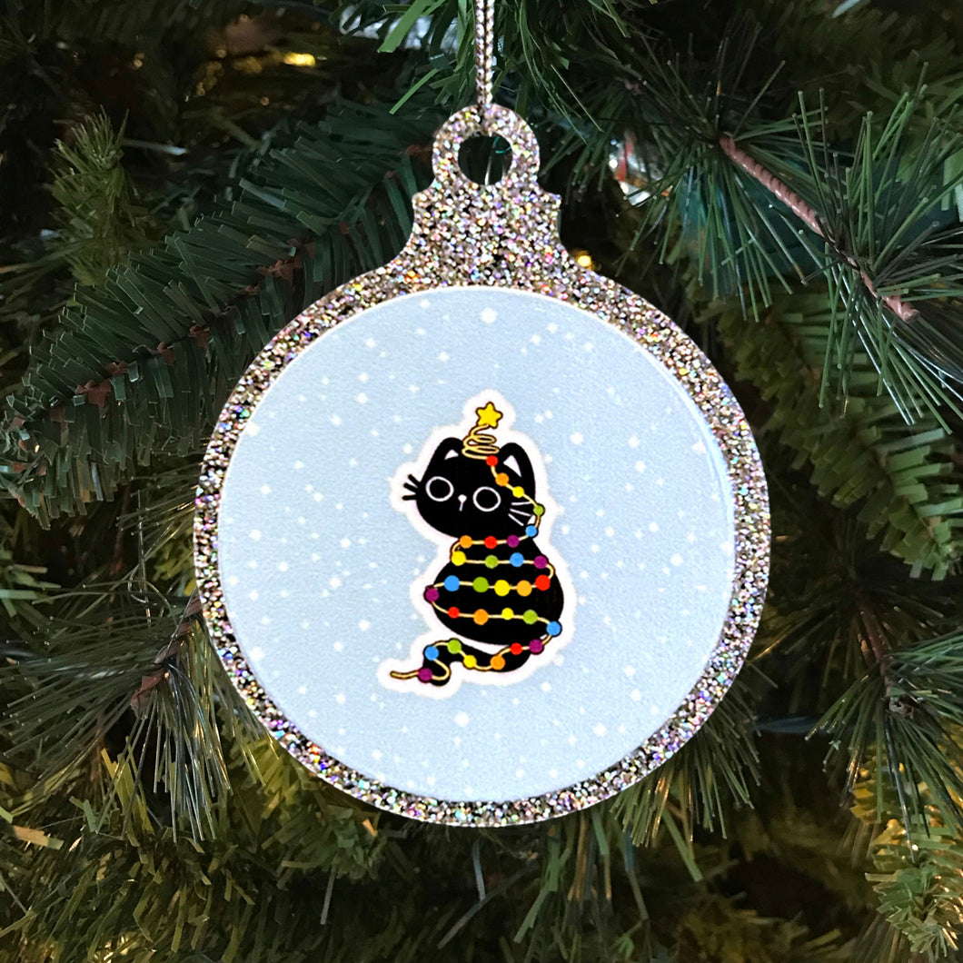 A sparkly Christmas bauble with a black cat tangled in rainbow-coloured fairy lights. The cat sits with a star on its head, looking adorable against a snowy background, hanging on a Christmas tree.