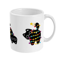 Load image into Gallery viewer, Right view of a white ceramic mug showing a playful black cat wrapped in rainbow-coloured Christmas lights, its tail coiled and star perched on top.