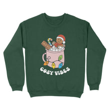 Load image into Gallery viewer, Bottle Green sweatshirt featuring retro text reading &#39;cosy vibes&#39;. The image shows a mug of hot chocolate with marshmallows and a gingerbread man wearing a Santa hat. A candy cane in the mug and lights around the mug are the colours of the rainbow pride flag.
