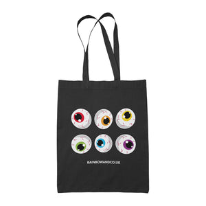 A black tote bag showcasing a collection of six cartoonish eyeballs arranged in two rows. Each eyeball has a unique colour: red, orange, yellow, green, blue, and purple. The text "RAINBOWANDCO.UK" is placed underneath the design, with a banner stating "8 IDENTITIES AVAILABLE".