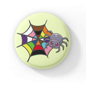 A circular badge featuring a grey spider with pink eyes on a web coloured in the rainbow colours, representing the LGBTQ+ pride flag. The badge has a light green background.