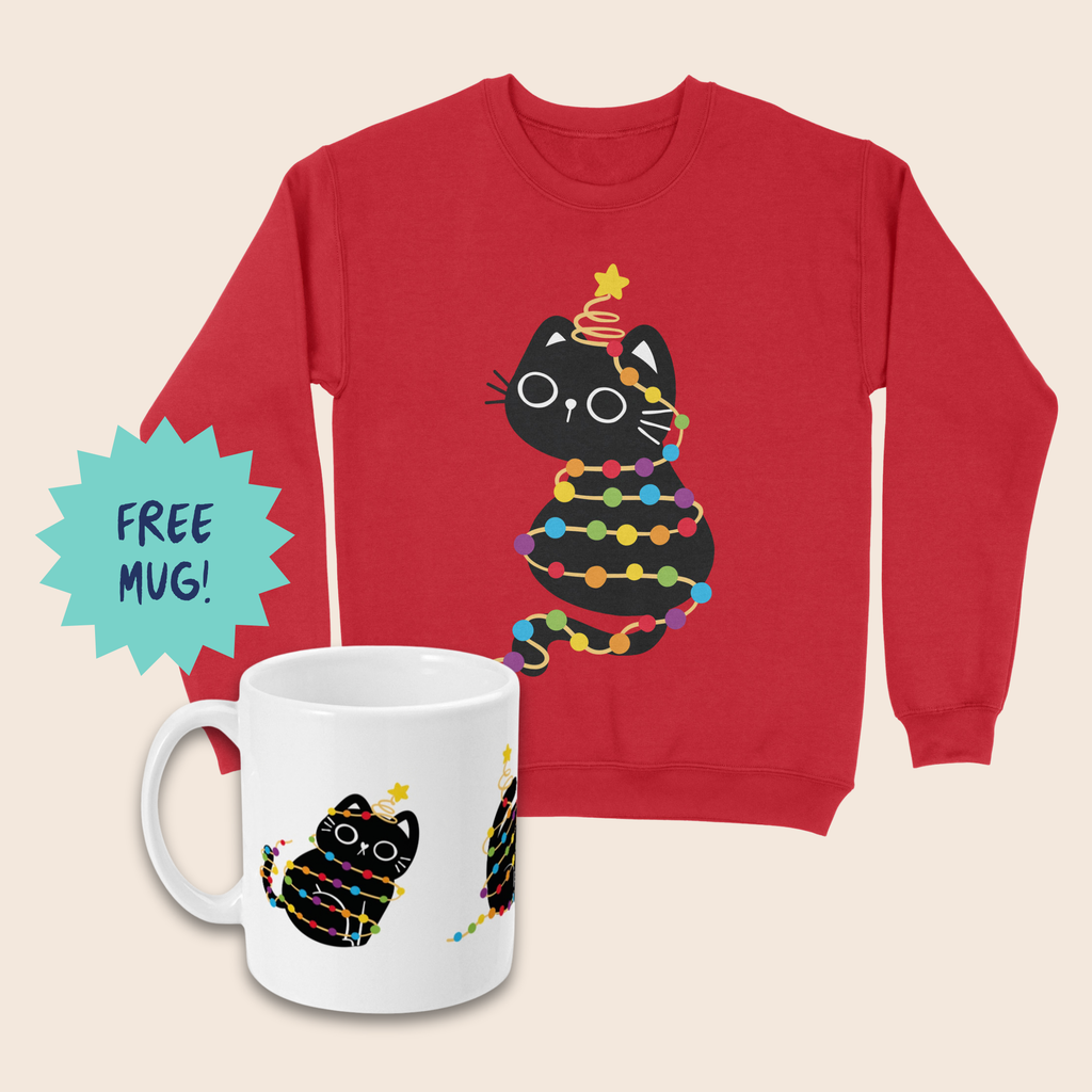 Red Christmas jumper and matching white mug featuring a black cat wrapped in rainbow-coloured fairy lights with a yellow star above its head, arranged on a cream background. A turquoise starburst beside the mug reads “FREE MUG!”