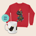 Red Christmas jumper and matching white mug featuring a black cat wrapped in rainbow-coloured fairy lights with a yellow star above its head, arranged on a cream background. A turquoise starburst beside the mug reads “FREE MUG!”