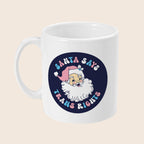 White ceramic mug with a dark navy circle featuring a vintage-style Santa illustration wearing a pink hat. Surrounding Santa is pastel bubble text that reads: “Santa Says Trans Rights.”
