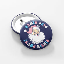 Load image into Gallery viewer, 38mm Santa Says Trans Right Badge - the badge is navy blue with text in the colours of the transgender flag and a graphic illustration of Santa Claus