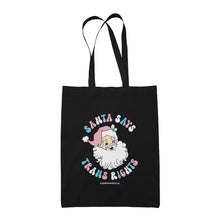 Load image into Gallery viewer, Black cotton tote bag featuring the slogan Santa Says Trans Rights with an image of Santa Claus. The text is in the colours of the transgender flag; pink, blue, and white.