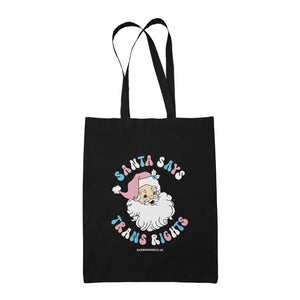 Black cotton tote bag featuring the slogan Santa Says Trans Rights with an image of Santa Claus. The text is in the colours of the transgender flag; pink, blue, and white.