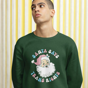 Young man wearing a bottle green sweatshirt with a Santa Says Trans Rights motif in the colours of the Transgender flag