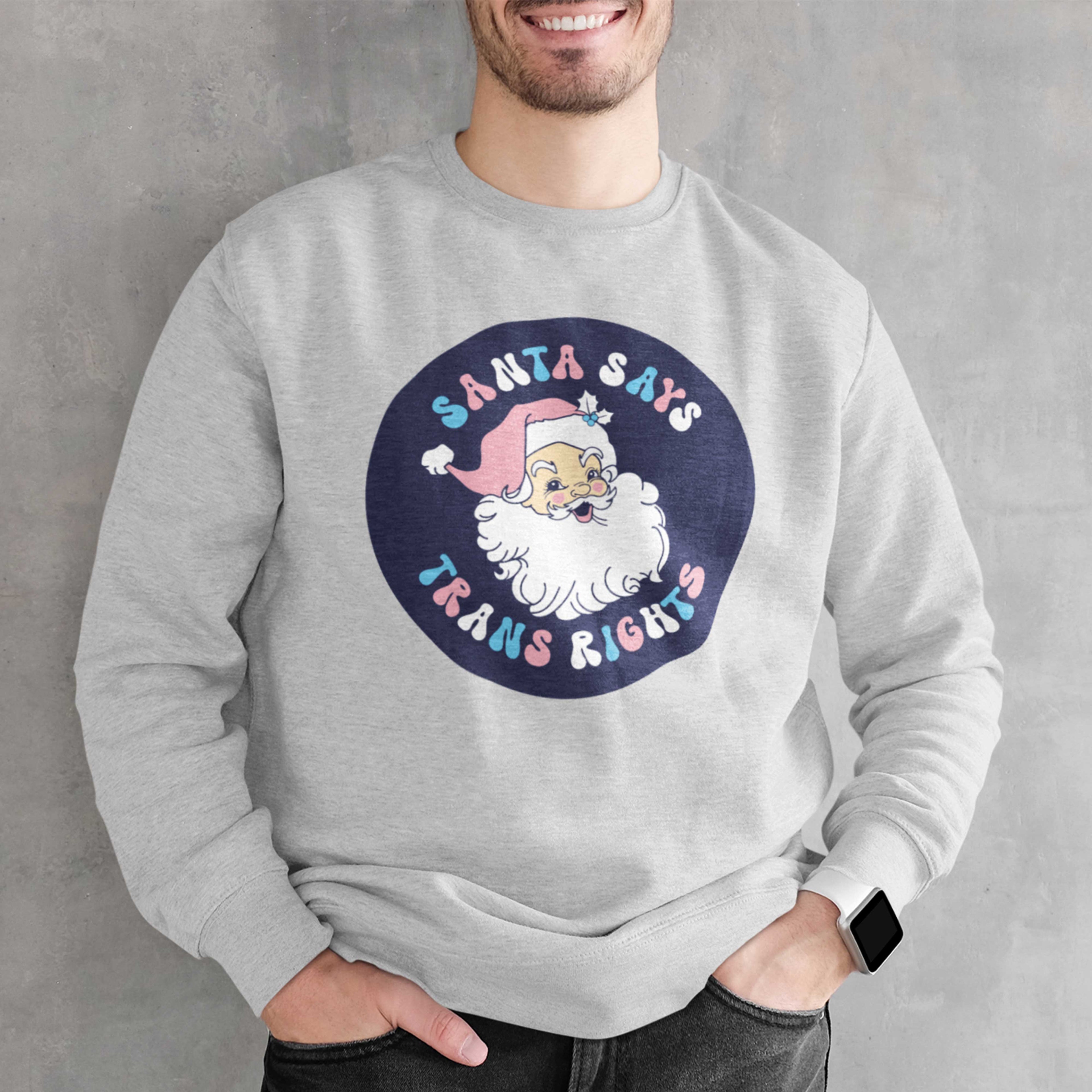 Young man wearing a heather grey sweatshirt with a Santa Says Trans Rights motif in the colours of the Transgender flag