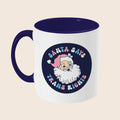 A white ceramic mug with a navy blue handle and interior. The design features a retro-style Santa Claus illustration and the phrase “Santa Says Trans Rights” in pastel tones, with the text curving around the image.