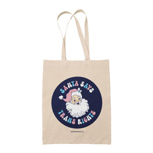 Load image into Gallery viewer, Natural cotton tote bag featuring the slogan Santa Says Trans Rights with an image of Santa Claus on a navy blue circle. The text is in the colours of the transgender flag; pink, blue, and white.