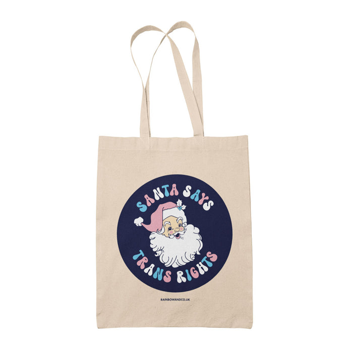 Natural cotton tote bag featuring the slogan Santa Says Trans Rights with an image of Santa Claus on a navy blue circle. The text is in the colours of the transgender flag; pink, blue, and white.