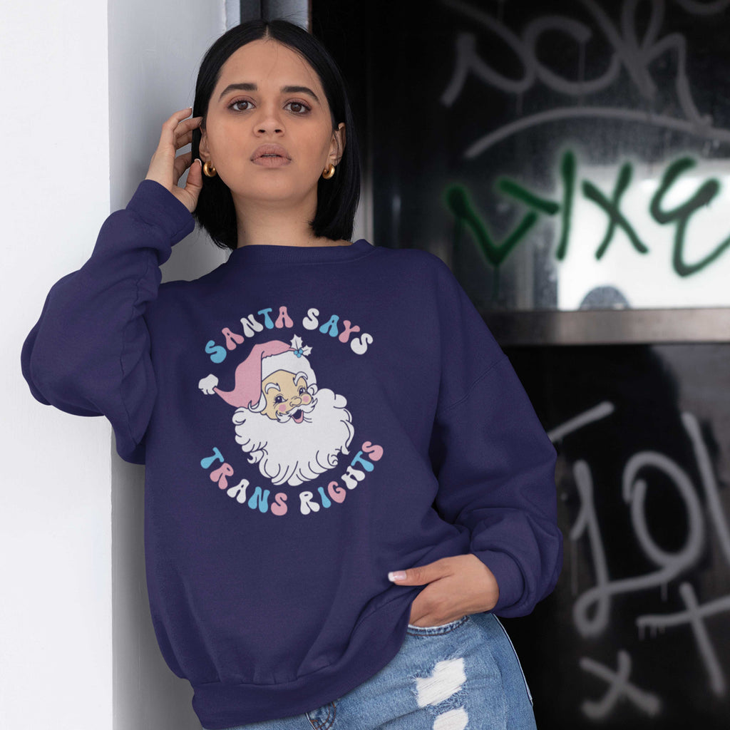 Young woman wearing an Oxford Navy sweatshirt with a Santa Says Trans Rights motif in the colours of the Transgender flag