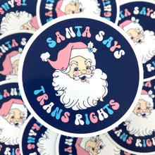 Load image into Gallery viewer, 75mm circular vinyl sticker with navy blue background and text reading Santa Says Trans Rights with an illustration of Santa Claus