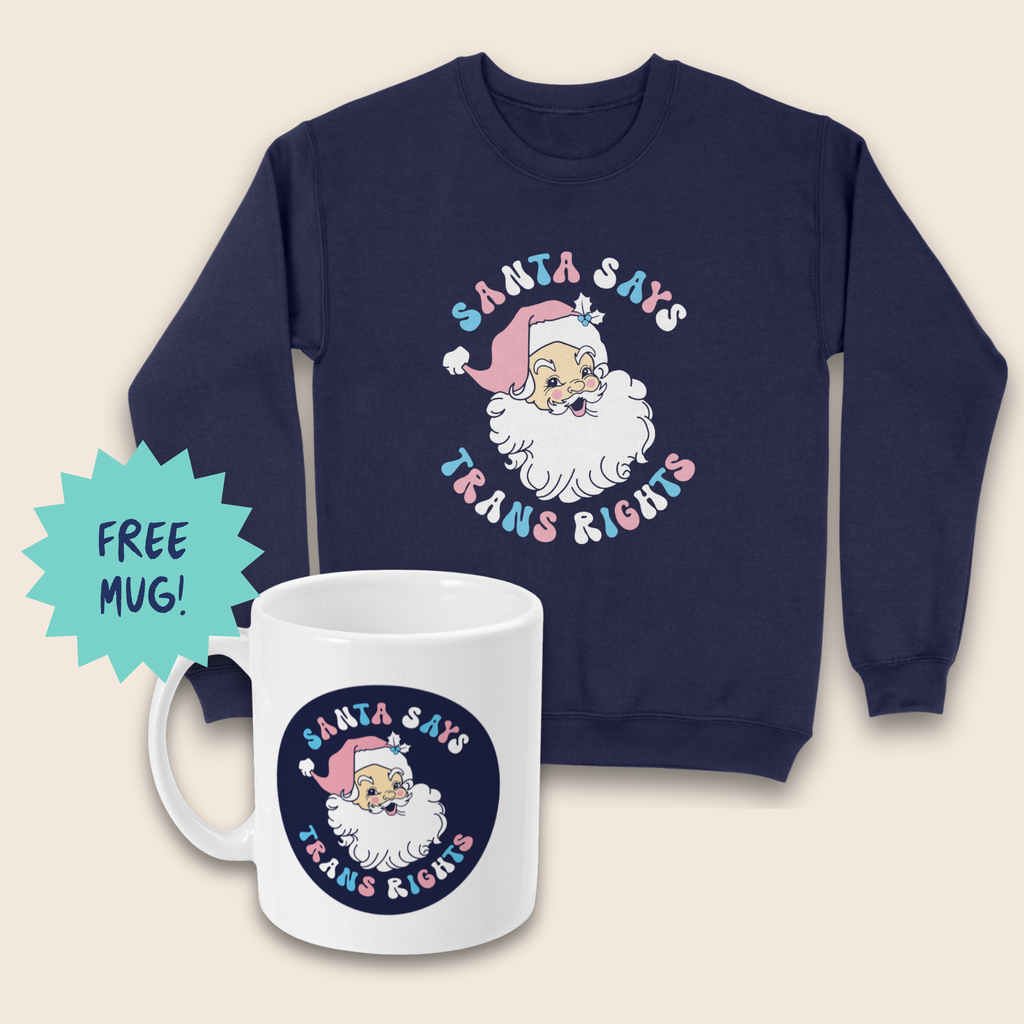 Navy sweatshirt and white mug featuring Santa’s face with “Santa Says Trans Rights” lettering in pink, blue and white, arranged on a cream background. A turquoise starburst beside the mug reads “FREE MUG!”