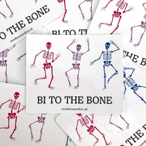 A pile of gloss stickers. Each sticker features three dancing skeletons in the colours of the bisexual flag and the slogan 'Bi To The Bone'