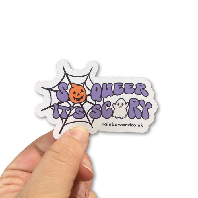 Glossy sticker featuring the phrase 'So Queer It's Scary' being held between a persons thumb and forefinger.