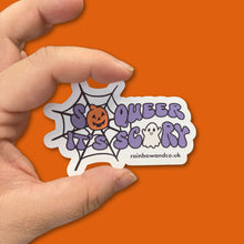 Load image into Gallery viewer, Glossy sticker featuring the phrase &#39;So Queer It&#39;s Scary&#39; being held between a persons thumb and forefinger against an orange background.