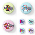 A collection of circular badges, each featuring a cute grey spider with pink eyes on a web coloured in various pride flag colours, including asexual, bisexual, gay, lesbian, non-binary, pansexual, rainbow, and transgender pride flags. Each badge has a different pastel background colour.