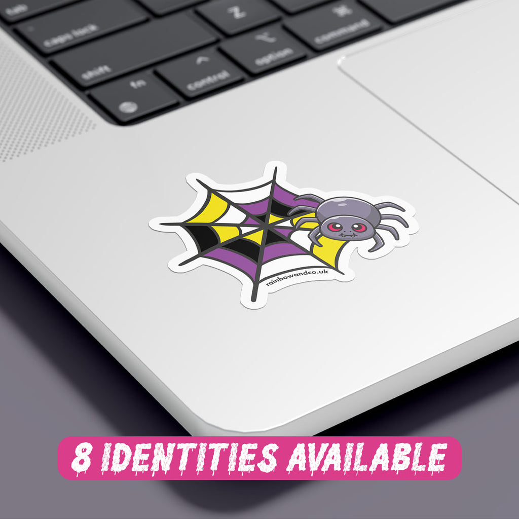 A colourful sticker featuring a cartoon spider with red eyes, resting on a spider web with a pattern that combines black, yellow, white, and purple colours, representing the non binary flag. The sticker is placed on the corner of a silver laptop, showcasing its vibrant design against the sleek surface. At the bottom, there is text in a playful pink font that reads "8 Identities Available."