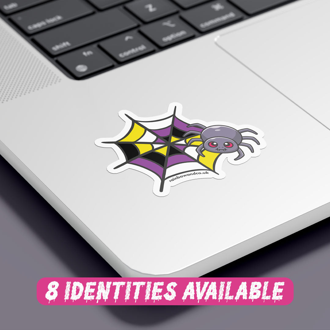 A colourful sticker featuring a cartoon spider with red eyes, resting on a spider web with a pattern that combines black, yellow, white, and purple colours, representing the non binary flag. The sticker is placed on the corner of a silver laptop, showcasing its vibrant design against the sleek surface. At the bottom, there is text in a playful pink font that reads "8 Identities Available."