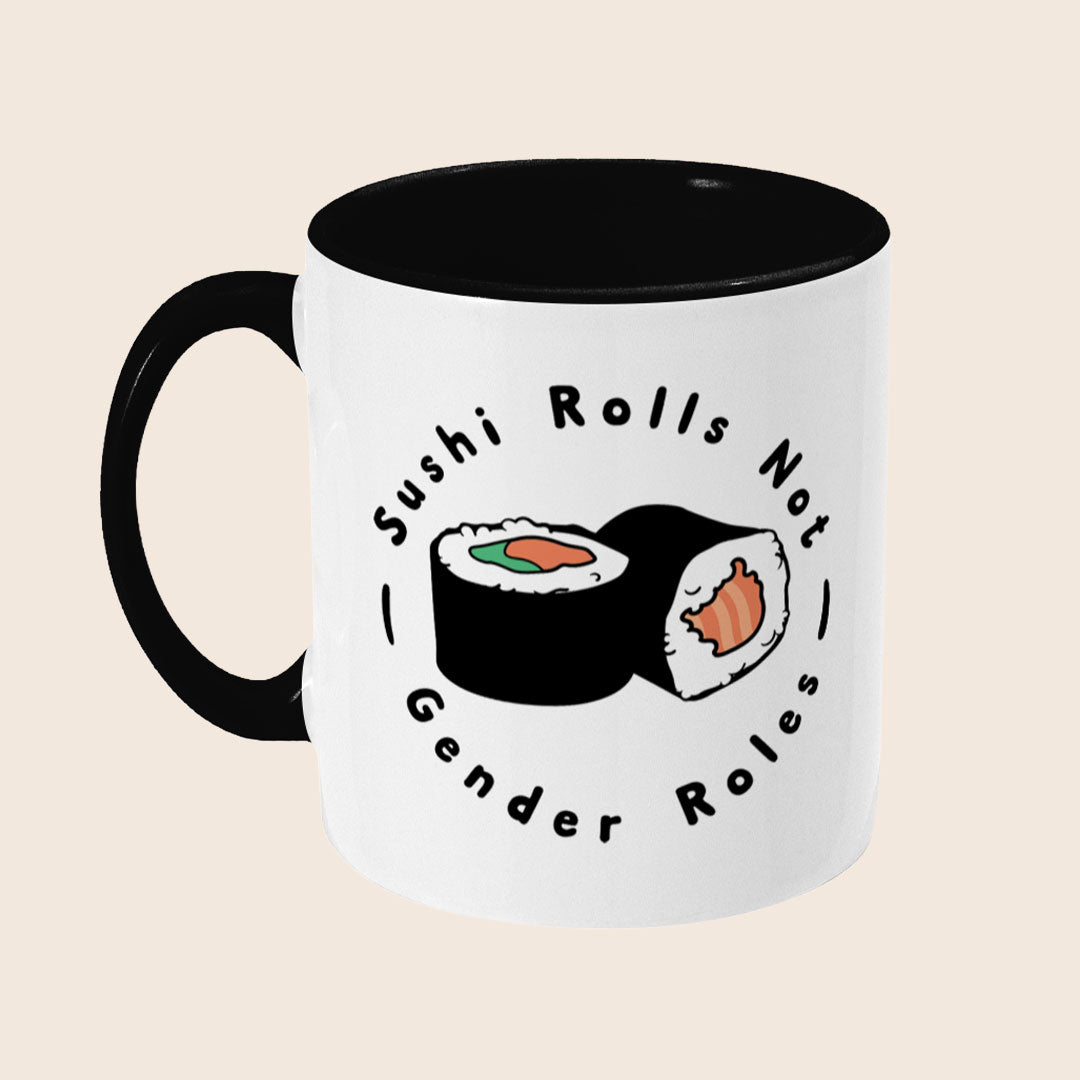 A white ceramic mug with a black handle and interior. The design shows two sushi rolls in the centre, framed by the phrase “Sushi Rolls Not Gender Roles” in a bold black font.