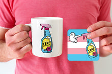 Load image into Gallery viewer, A white ceramic mug featuring a colourful &quot;TERF Repellent&quot; design with a spray bottle, alongside a matching square coaster with the same design over a transgender pride flag background. The mug is held by a person wearing a pink shirt.