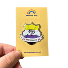 Load image into Gallery viewer, White hand holding up an enamel pin on a yellow backing card. The pin is in the shape of a shield with a banner across it&#39;s front. Banner reads They of Honor. The background of the pin is the non binary pride flag and there is a jewel icon in the centre. The jewel and banner are filled with white glitter.