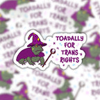 Toadally for Trans Rights wizard toad sticker centred over a blurred repeating background of the same purple, green and white sticker design.