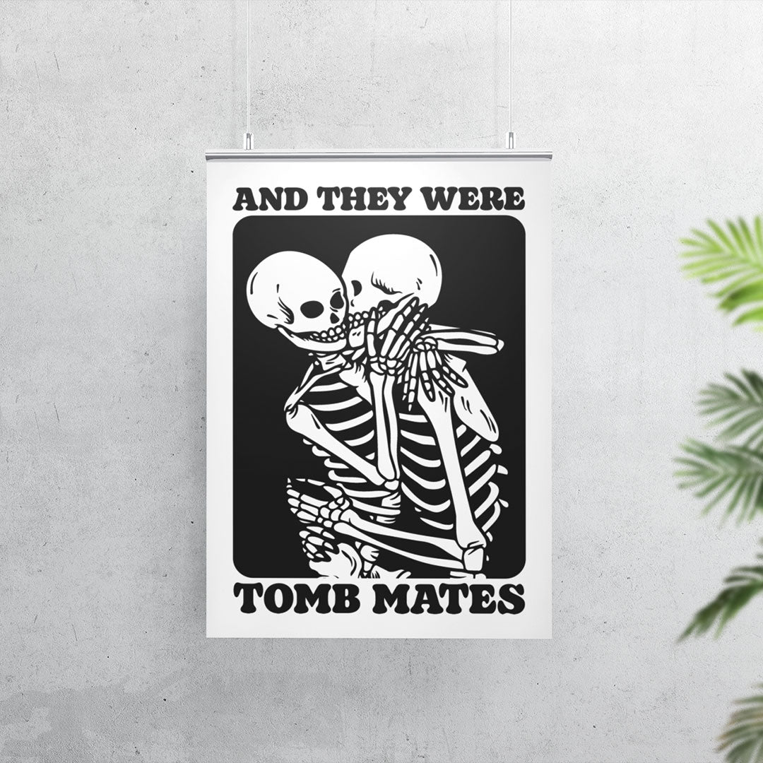 A poster of "And They Were Tomb Mates" featuring two skeletons in a close, affectionate embrace, printed in black and white. The poster hangs on a minimalist concrete wall, suspended from a metallic clip. A potted plant with green leaves is slightly visible on the right side of the image, adding a touch of greenery to the setting.