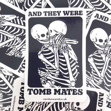 Load image into Gallery viewer, A pile of glossy stickers with one sticker in the foreground. The stickers show two skeletons embracing and the text &#39;And They Were Tomb Mates&#39;