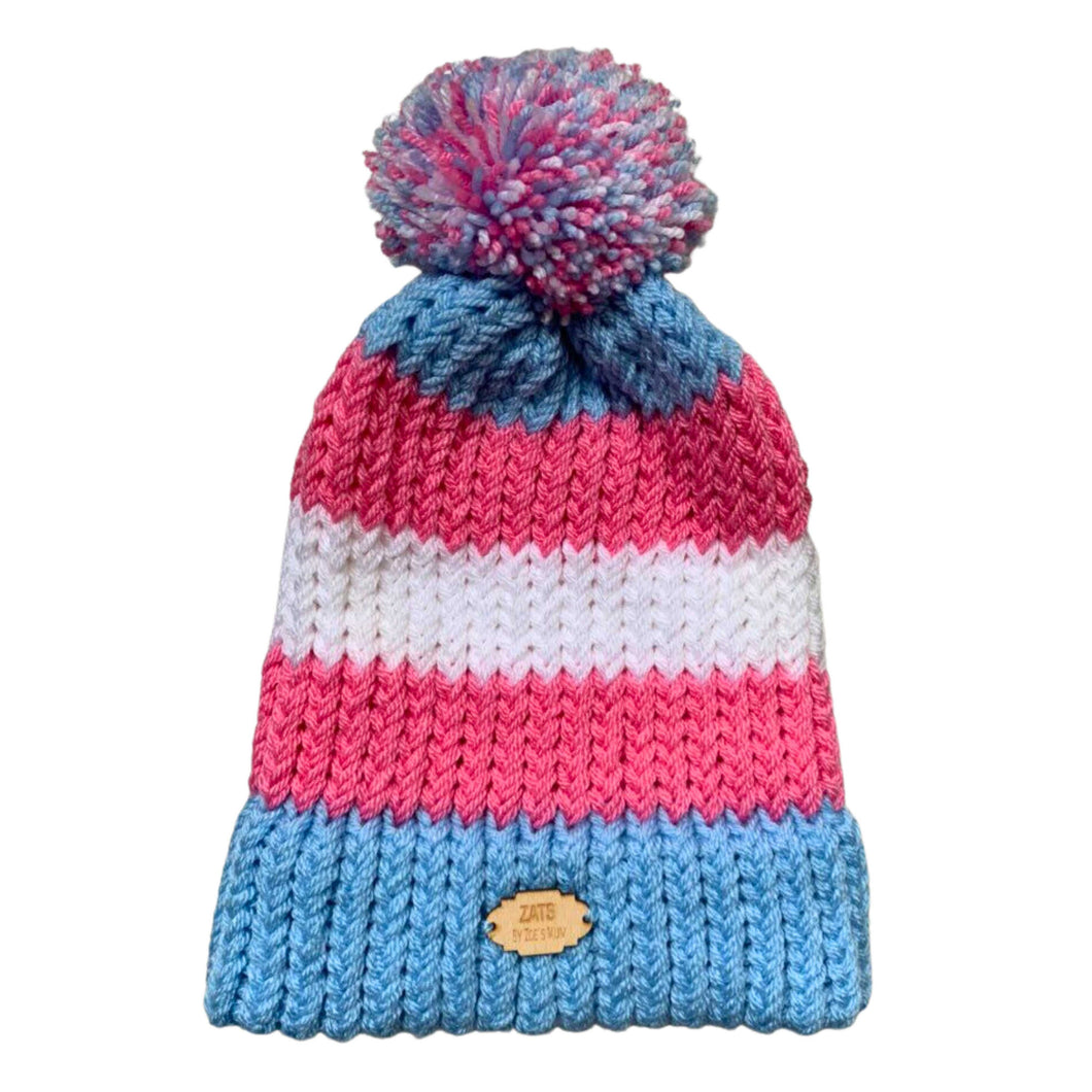Striped knitted bobble hat in the colours of the Transgender pride flag laying flat.