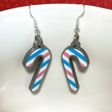 Load image into Gallery viewer, Silver glitter candy cane dangle earrings hung over the edge of a mug. The stripes on the candy cane are those of the Transgender flag; blue, pink, and white.