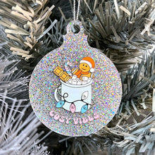 Load image into Gallery viewer, Close up of a white Christmas tree displaying a silver glitter bauble featuring retro text reading &#39;cosy vibes&#39;. The image shows a mug of hot chocolate with marshmallows and a gingerbread man wearing a Santa hat. A candy cane in the mug and lights around the mug are the colours of the transgender pride flag.