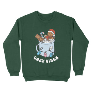 Bottle Green sweatshirt featuring retro text reading 'cosy vibes'. The image shows a mug of hot chocolate with marshmallows and a gingerbread man wearing a Santa hat. A candy cane in the mug and lights around the mug are the colours of the transgender pride flag.
