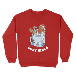 Fire Red sweatshirt featuring retro text reading 'cosy vibes'. The image shows a mug of hot chocolate with marshmallows and a gingerbread man wearing a Santa hat. A candy cane in the mug and lights around the mug are the colours of the transgender pride flag.