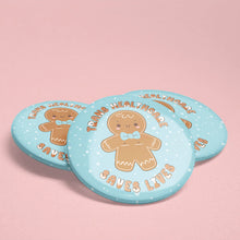 Load image into Gallery viewer, A set of three pastel blue 38mm badges with a smiling gingerbread person in the centre, featuring top surgery scars and a light blue bowtie. The text around the gingerbread reads &quot;Trans Healthcare Saves Lives.