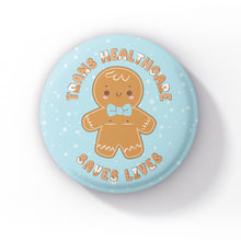 Load image into Gallery viewer, A close-up of a pastel blue 38mm badge, featuring a smiling gingerbread person with top surgery scars and a light blue bowtie. The text &quot;Trans Healthcare Saves Lives&quot; wraps around the design in a playful font.