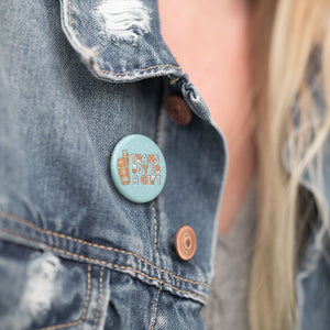 A close-up of a "Trans Joy is a Gift" badge pinned on a denim jacket, accentuating the badge against the rugged texture of the denim.